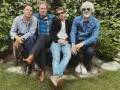Un grupo de cuatro hombres con ropa informal sentados en un banco, todos con una gran sonrisa.