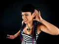 Fatima Hajji, con su característico estilo, escucha atentamente, con una mano en la oreja y una sonrisa pícara.