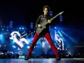 Matt Bellamy de Muse España, con pantalones rojos y chaqueta negra, toca la guitarra en un escenario iluminado por luces azules y pantallas gigantes.