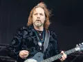 Rich Robinson, guitarrista con cabello largo y barba, luce un saco negro con estampado floral azul y varias cadenas.