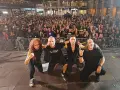 La banda Syberia posa con su público. Los músicos, con atuendos oscuros, se arrodillan mientras una multitud enardecida los aclama.