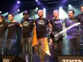 Seis músicos de maizu rock en el escenario, abrazados y sonriendo. Uno sostiene una guitarra eléctrica.