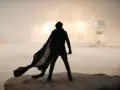 Silueta de un hombre con capa ondeando, observando una explosión en el desierto. La banda sonora de Dune evoca esta escena épica.