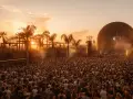 Multitud en el festival Sophie, disfrutando del atardecer con palmeras y una gran esfera como escenario.