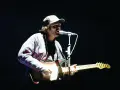 Neil Halstead, con gorra y camisa a cuadros, toca la guitarra y canta en un concierto.
