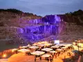 Un impresionante festival Porriño ilumina una cantera con luces moradas. Gente reunida bajo sombrillas blancas, disfrutando del evento.