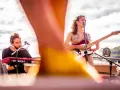 Maria y Feu, una banda en vivo, tocan en un escenario al aire libre. Ella canta y toca la guitarra, él en los teclados.