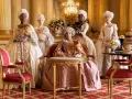 Cinco damas con pelucas empolvadas y vestidos de época, algunas con perros, evocan la banda sonora de los Bridgerton en un salón dorado.