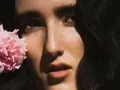 Primer plano de Judeline, cantante, con una flor rosa junto a su rostro.