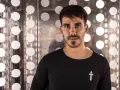 Raúl Pacheco, DJ, posa con una camiseta negra frente a un fondo metálico con círculos blancos brillantes.