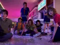 Los personajes de Stranger Things, con Eleven al frente, sentados en el suelo de un centro comercial, evocando las icónicas canciones de la serie.