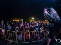 Un cantante con tatuajes canta en un concierto de charca rock. El público, animado, se agolpa tras una valla amarilla.