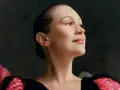 Joanna Newsom, con su cabello recogido y un vestido negro con detalles brillantes, mira hacia arriba con una expresión serena.