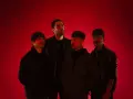 Cuatro hombres posan ante un fondo rojo vibrante. Parecen una banda, quizás "los flamingos", con sus miradas intensas y atuendos modernos.