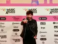 Hombre con chaqueta de cuero negro señala a la cámara en una alfombra roja de Los40 Music Awards. ¡Parece que ha pescado el premio!