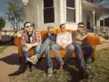Cuatro hombres sentados en un sofá naranja, como si fueran **track dogs** esperando su próxima aventura.