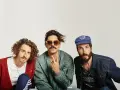 Tres hombres posan, uno con cárdigan rojo, otro con gafas de sol y chaqueta bomber, y el tercero con gorra azul. Parecen un grupo de música, quizás el cantante sexy de Zebras.
