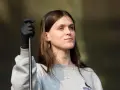 Ethel Cain, con guantes negros y un collar de cruz, mira hacia un lado con una expresión pensativa.