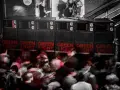 Altavoces apilados con luces rojas "GREEN LIGHT" y gente borrosa bailando. Un sistema de sonido que parece dar problemas.