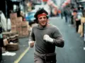 Rocky Balboa corre por la calle, con su icónica banda roja en la cabeza. La banda sonora de Rocky resuena en tu mente.