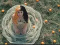Melanie Martinez, con su icónico cabello mitad naranja y mitad negro, rodeada de naranjas en un campo. ¡Atentos a los próximos eventos de Melanie Martinez!
