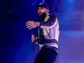 Nicky Jam, con su gorra y chaqueta llamativa, canta en un concierto en Granada, cautivando al público con su energía.