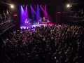 Un concierto en Guitar BCN ilumina el escenario con luces púrpuras mientras una multitud entusiasta graba el momento.