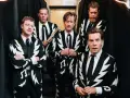 Los miembros de The Hives posan con trajes llamativos. Uno sostiene baquetas, listo para la acción.
