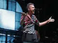 El cantante de Vetusta Morla Sevilla canta apasionadamente en un concierto, con las manos extendidas y un micrófono frente a él.