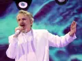 Un hombre con traje blanco canta en un escenario con luces vibrantes. ¡Murcia on!