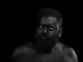 Hombre con el rostro y cuerpo cubiertos de pintura negra, ojos penetrantes. Parece un guerrero ancestral, don fluor.