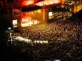 Multitudinaria asistencia a conciertos en julio. Una banda toca en un escenario iluminado ante miles de fans.