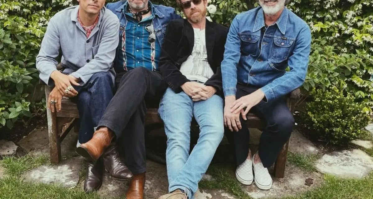 Un grupo de cuatro hombres con ropa informal sentados en un banco, todos con una gran sonrisa.