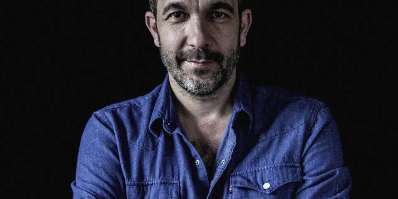 Hombre con barba y camisa vaquera azul, mirada directa. Podría ser DJ Coco listo para pinchar.