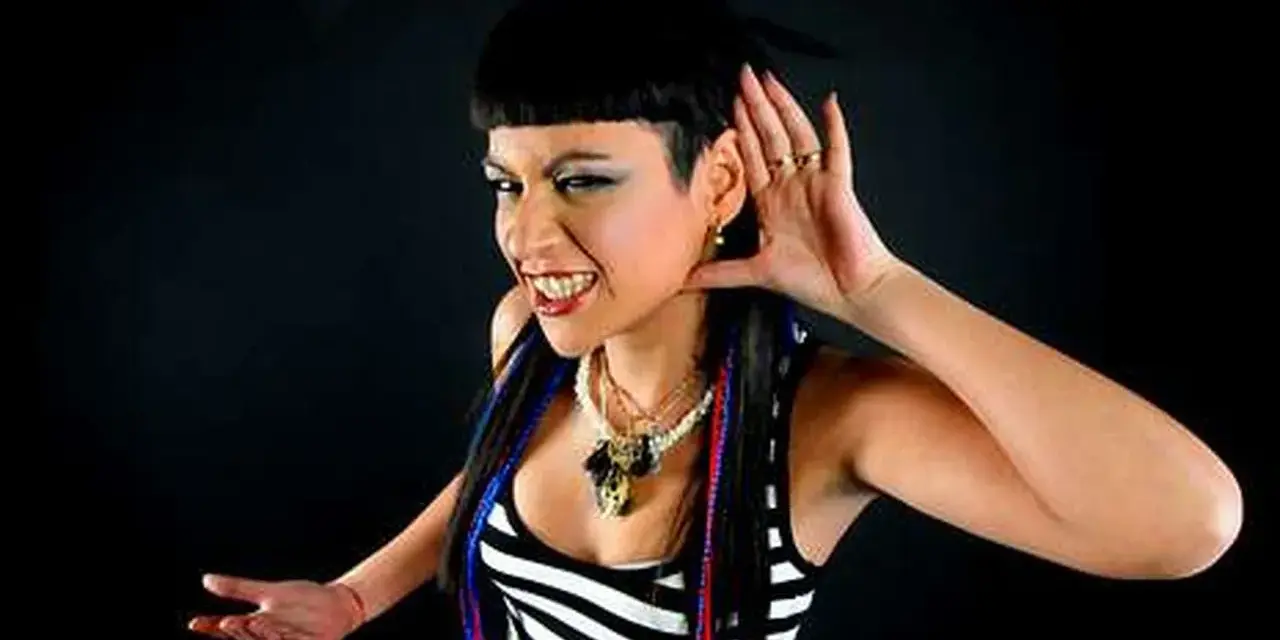 Fatima Hajji, con su característico estilo, escucha atentamente, con una mano en la oreja y una sonrisa pícara.