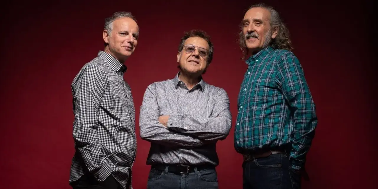 Los miembros de Els Pets posan sonrientes ante un fondo rojo.