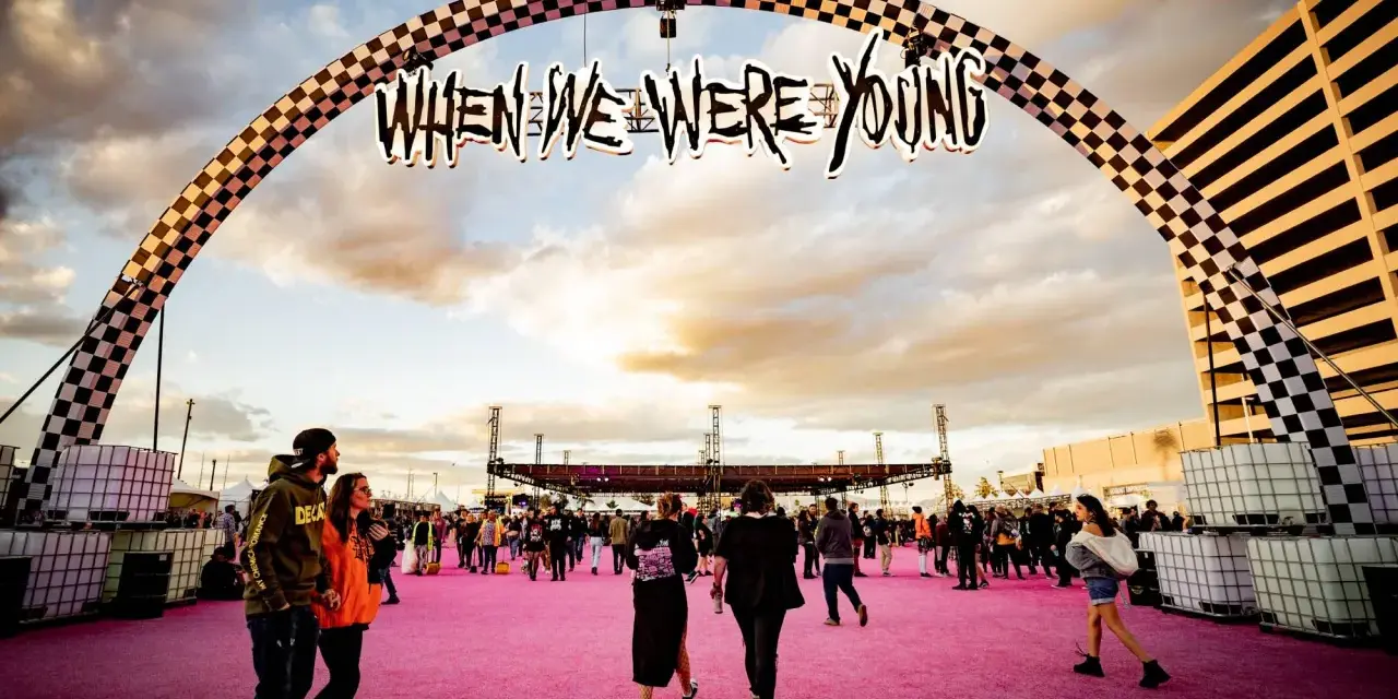 Gente camina bajo un arco con el letrero "When We Were Young Festival" sobre una alfombra rosa.