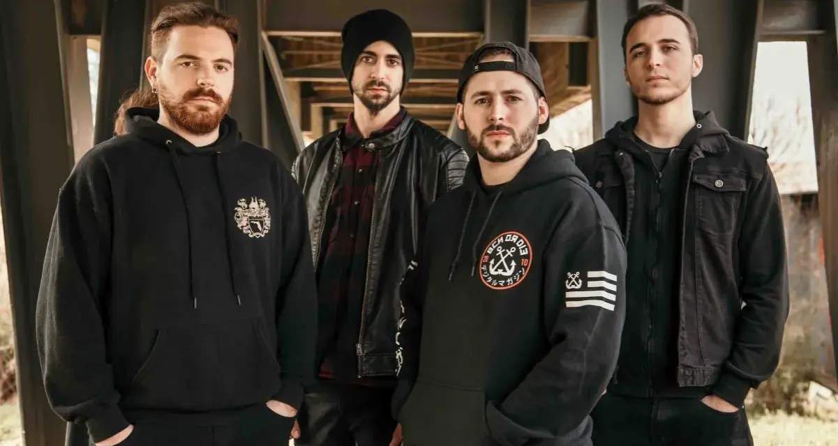 Cuatro hombres con sudaderas y chaquetas negras posan bajo una estructura metálica. Sus miradas intensas parecen **blaze out** con determinación.