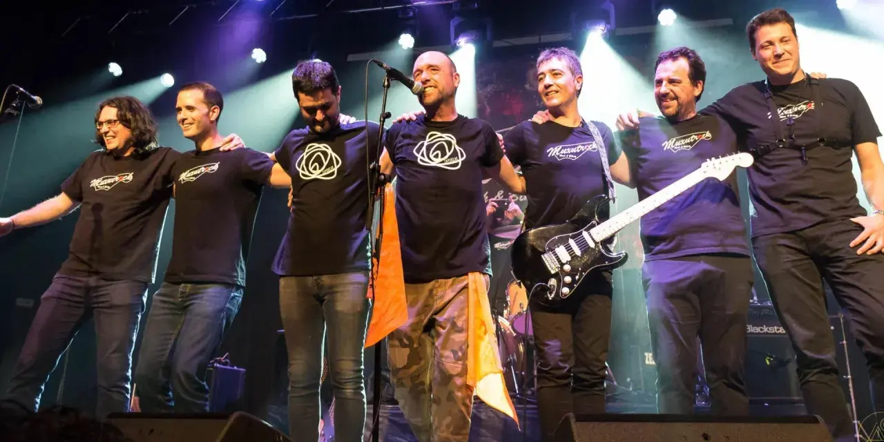 Seis músicos de maizu rock en el escenario, abrazados y sonriendo. Uno sostiene una guitarra eléctrica.