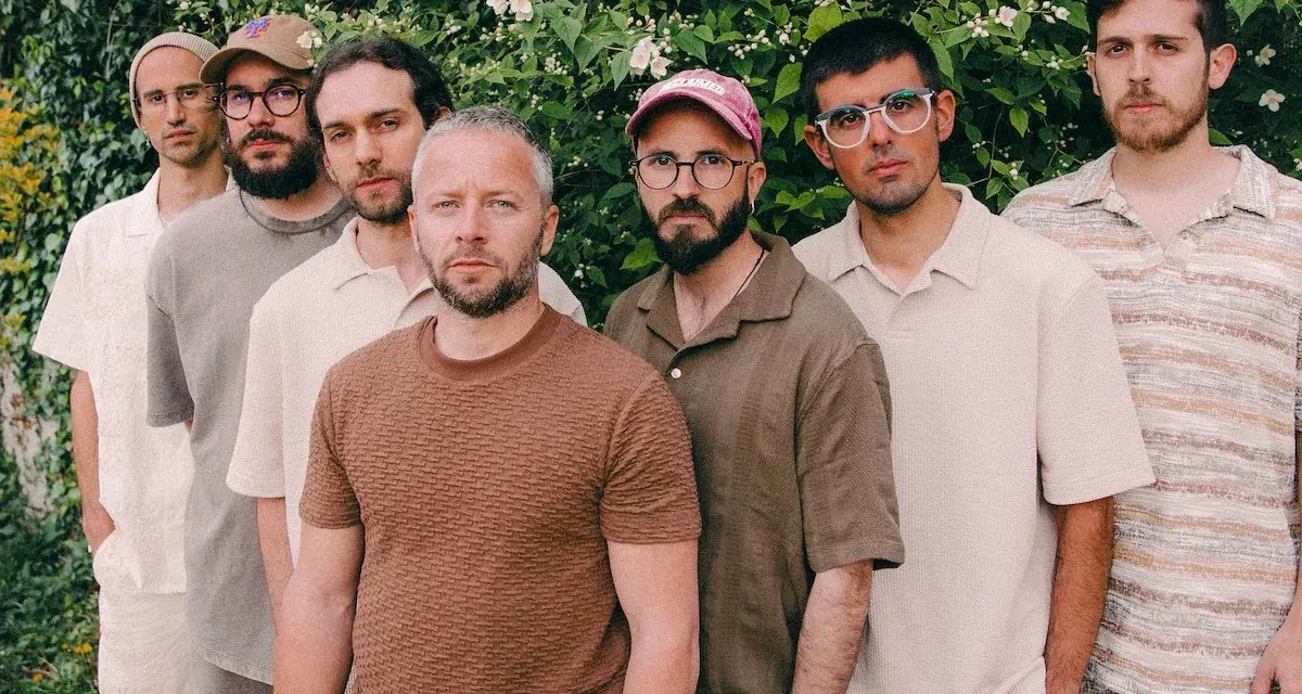 Los miembros de Oques Grasses posan juntos, con ropa de tonos tierra y un fondo de vegetación frondosa.