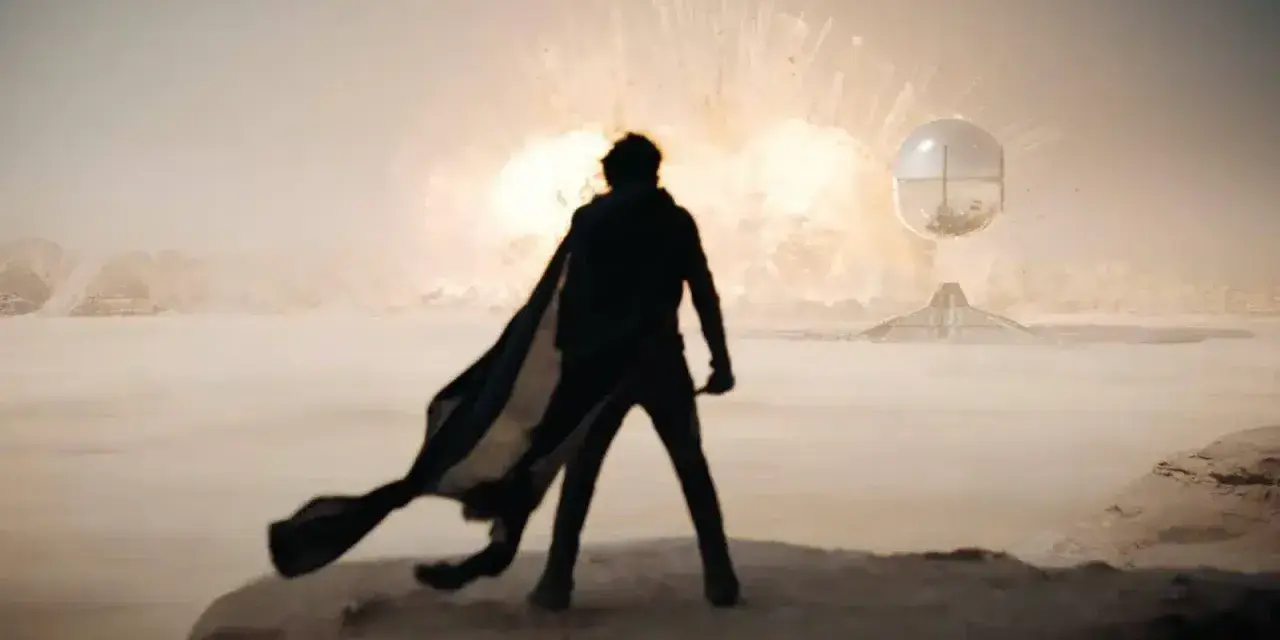 Silueta de un hombre con capa ondeando, observando una explosión en el desierto. La banda sonora de Dune evoca esta escena épica.