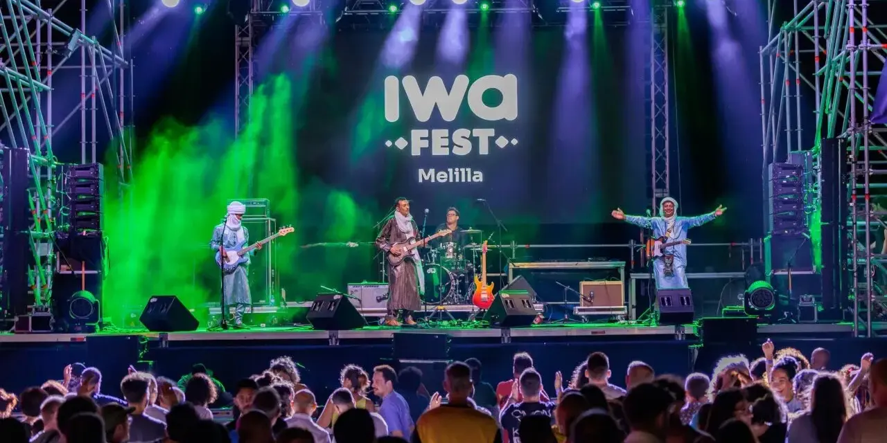 Banda tocando en el iwa fest de Melilla, con luces verdes y moradas, y una multitud disfrutando.