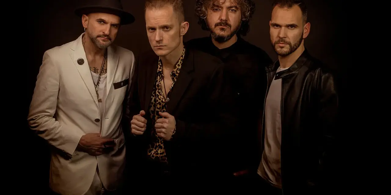 El grupo de embusteros posa con miradas intensas. Uno lleva sombrero y traje blanco, otro camisa de leopardo, y los otros dos, chaquetas oscuras.