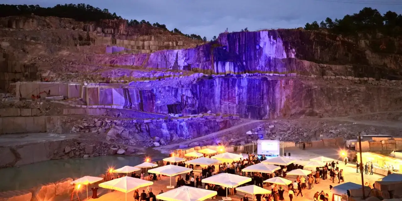 Un impresionante festival Porriño ilumina una cantera con luces moradas. Gente reunida bajo sombrillas blancas, disfrutando del evento.