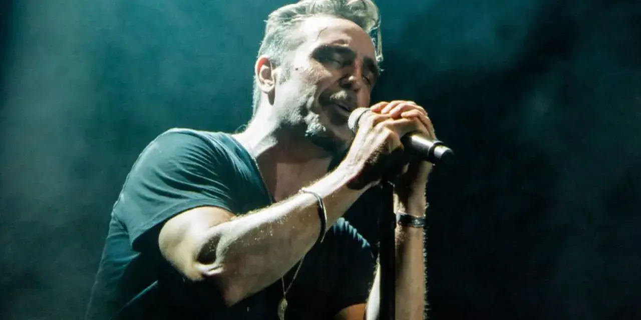 Un miembro de OBK canta apasionadamente en el escenario, iluminado por focos.