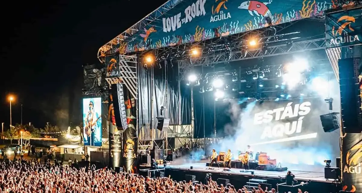 Multitud en concierto, luces brillantes y humo en el escenario. El cartel dice "Love to Rock".