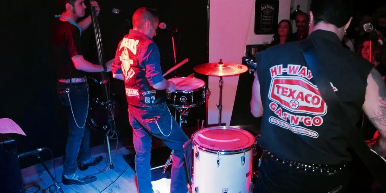 Un grupo de gatos locos en el escenario, tocando rock and roll con un contrabajo, batería y guitarra.