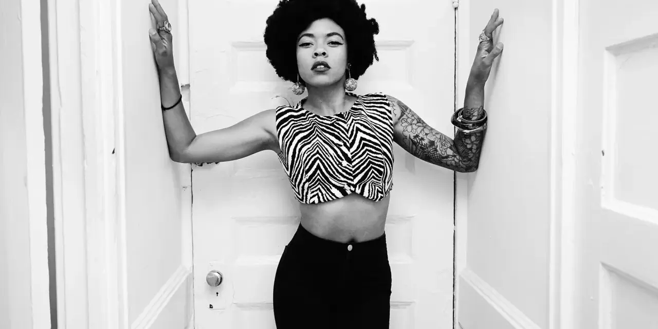 Nikki Hill, con su afro y top de cebra, posa con confianza entre puertas blancas.