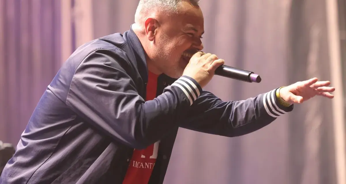 Juan Magán cantando en un escenario con micrófono y gesto animado.