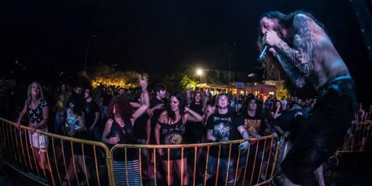 Un cantante con tatuajes canta en un concierto de charca rock. El público, animado, se agolpa tras una valla amarilla.